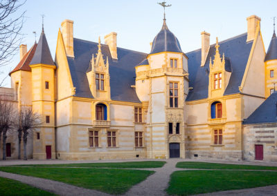 Vue du logis renaissance du château d’Ainay-le-Vieil depuis la cour d'honneur. Facade ensoleillée, toits en ardoise, fenêtres à meneaux, girouette en fonte