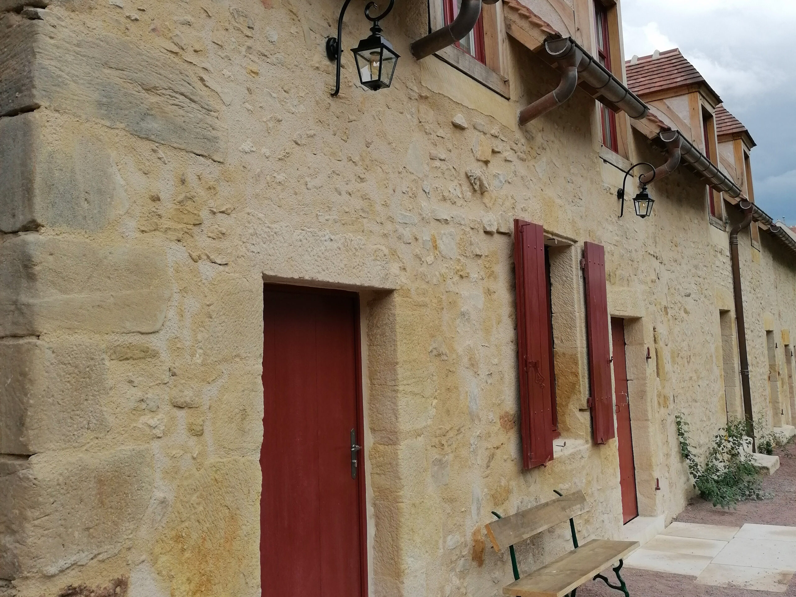 Château d&#039;Ainay-le-Vieil, gîte La Grange, façade avec porte d&#039;entrée, pierres apparentes et volets rouges